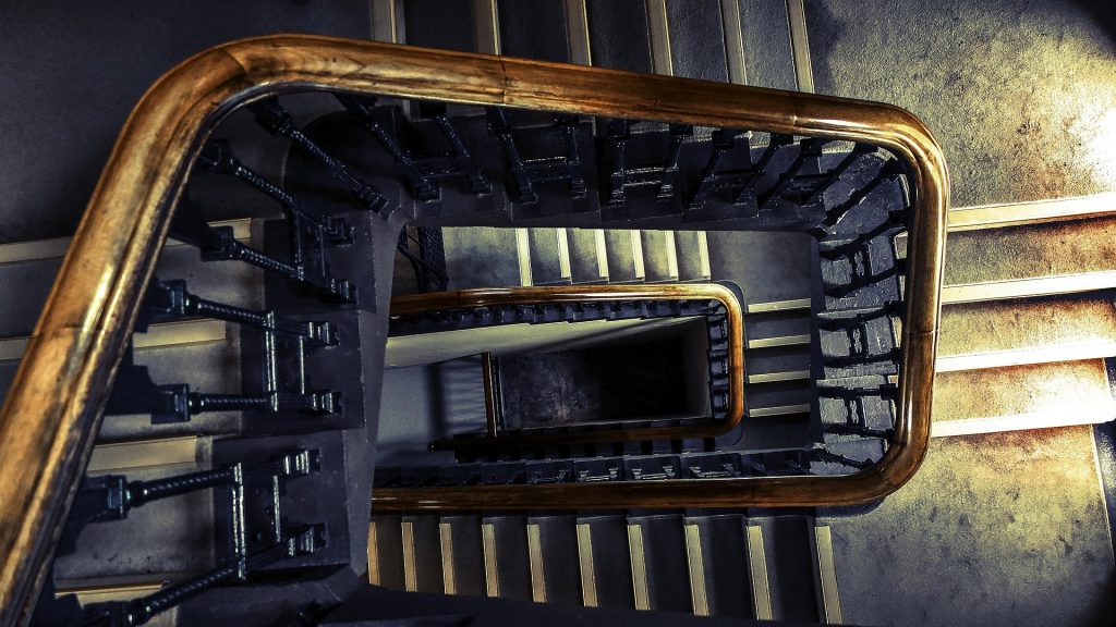 A staircase spiralling down with a wooden railing.